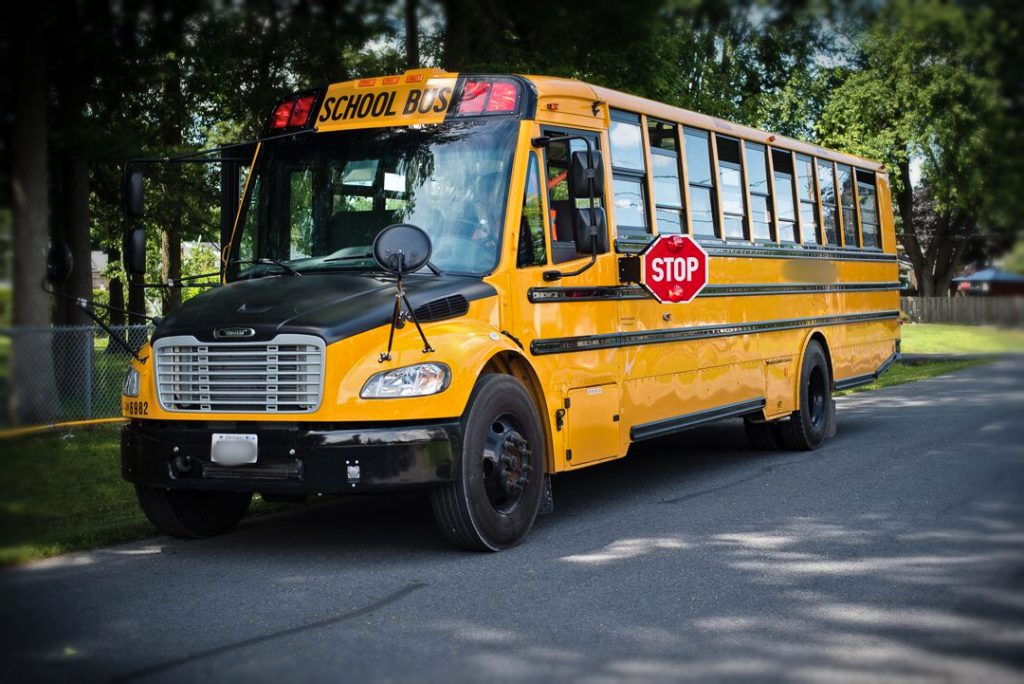 Yellow school bus on a paved road with RED stop sign out, green grass and trees in background