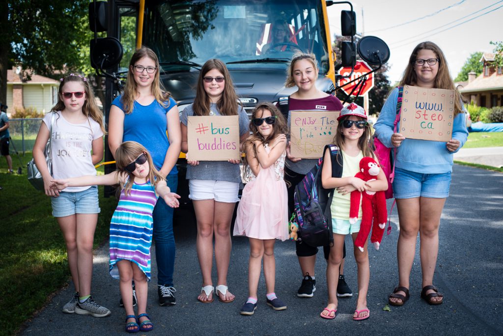 eight female students standing in front of parked bus holding various signs