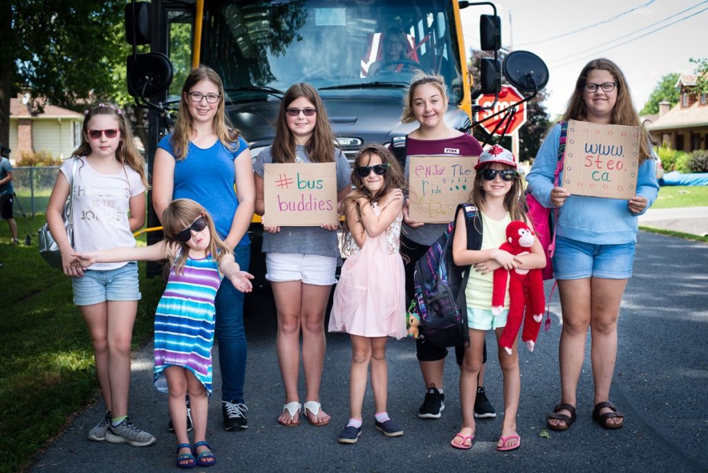 students standing in front of a big yellow bus